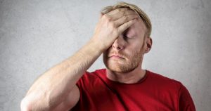 Man in red shirt holds head in pain